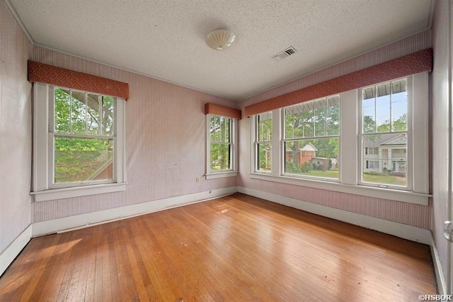 unfurnished room with baseboards, visible vents, hardwood / wood-style flooring, and a textured ceiling