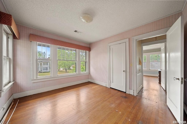 spare room featuring baseboards, visible vents, a textured ceiling, and wood-type flooring
