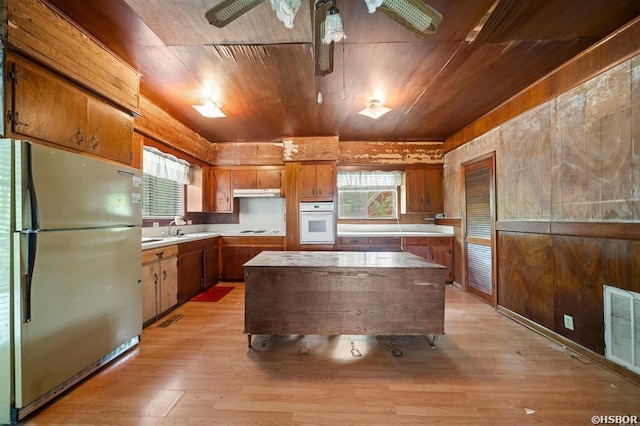 kitchen with visible vents, light countertops, freestanding refrigerator, white oven, and brown cabinetry