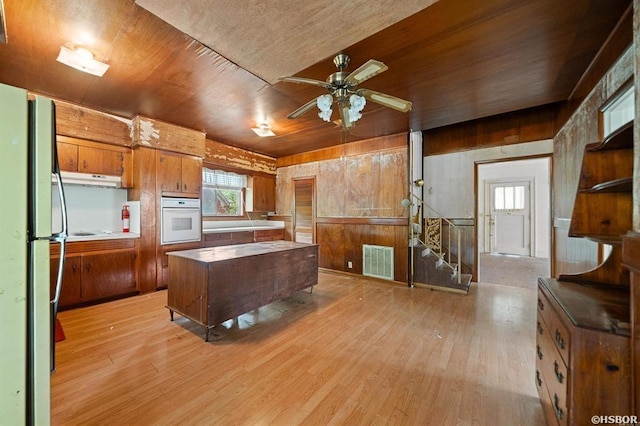 kitchen with white oven, brown cabinetry, a kitchen island, ceiling fan, and visible vents