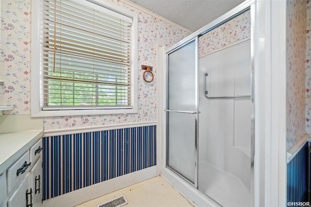 bathroom featuring a textured ceiling, a stall shower, a wainscoted wall, and wallpapered walls
