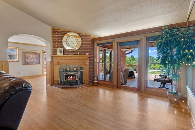 living area featuring visible vents, wood finished floors, vaulted ceiling, a textured ceiling, and a brick fireplace