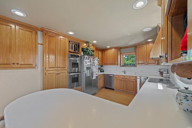kitchen with a peninsula, a sink, light countertops, appliances with stainless steel finishes, and decorative backsplash