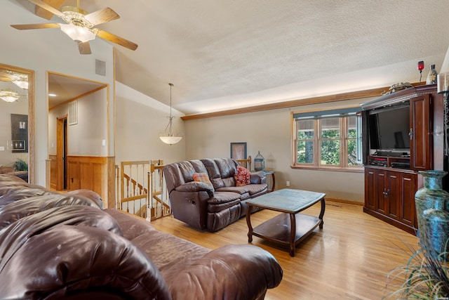 living area featuring visible vents, a wainscoted wall, light wood-style flooring, vaulted ceiling, and a textured ceiling