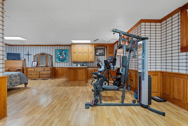 workout room with wallpapered walls, light wood-style flooring, and wainscoting