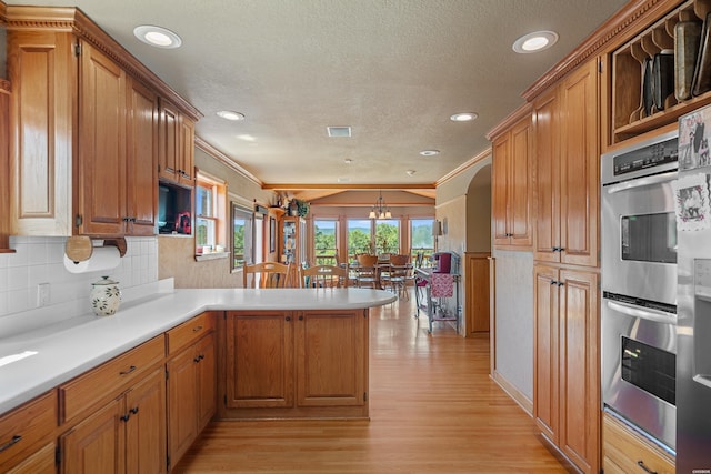 kitchen featuring double oven, a peninsula, light wood-style floors, light countertops, and brown cabinets