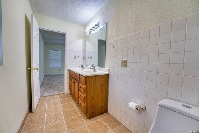 bathroom with tile walls, double vanity, toilet, a textured ceiling, and tile patterned floors