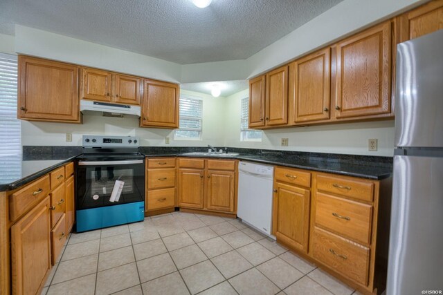 kitchen with appliances with stainless steel finishes, brown cabinetry, a sink, and under cabinet range hood