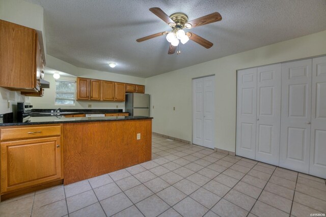 kitchen with a textured ceiling, dark countertops, freestanding refrigerator, and brown cabinets