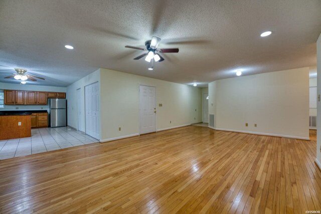 unfurnished living room featuring ceiling fan, light wood finished floors, a textured ceiling, and baseboards