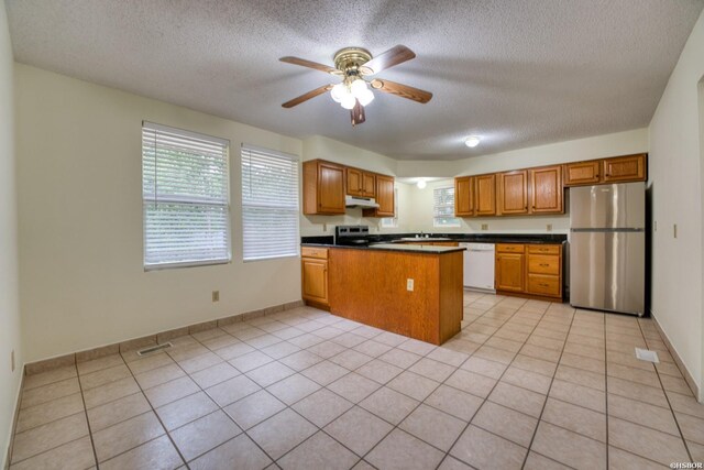 kitchen featuring appliances with stainless steel finishes, dark countertops, brown cabinetry, and a peninsula