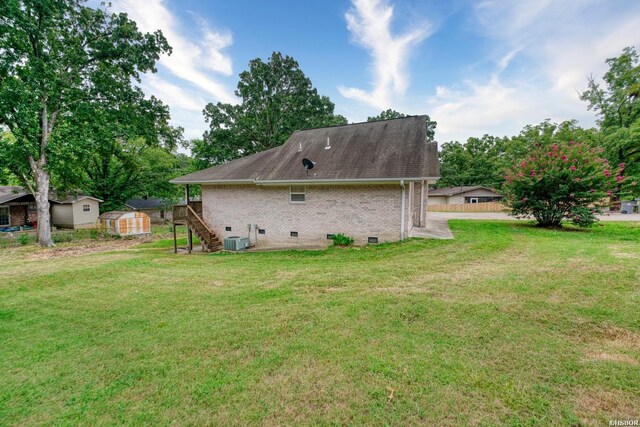 back of property featuring brick siding, an outdoor structure, stairs, a yard, and crawl space