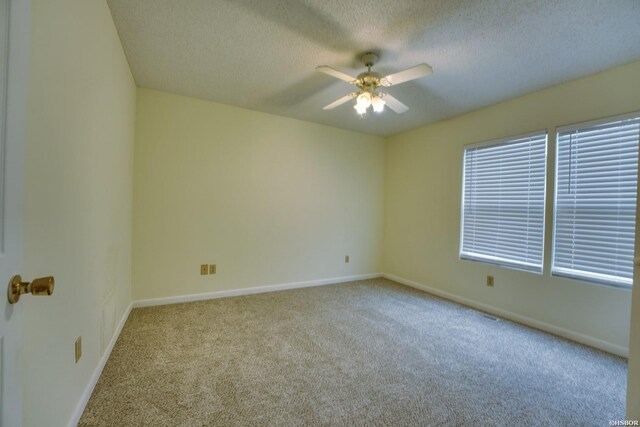 empty room with light carpet, a textured ceiling, a ceiling fan, and baseboards