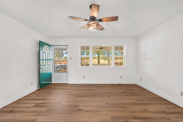 empty room with dark wood-style floors, a textured ceiling, baseboards, and a ceiling fan