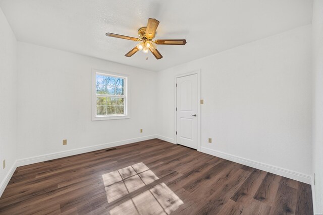 unfurnished room with dark wood-type flooring, a ceiling fan, and baseboards