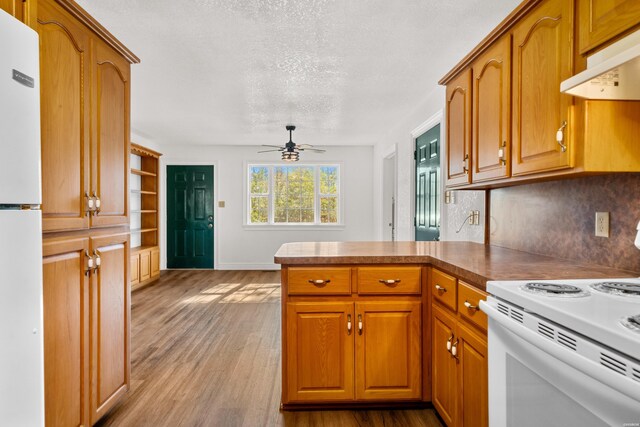 kitchen with white appliances, brown cabinetry, wood finished floors, and under cabinet range hood