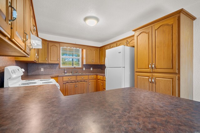 kitchen featuring white appliances, brown cabinetry, dark countertops, ventilation hood, and a sink