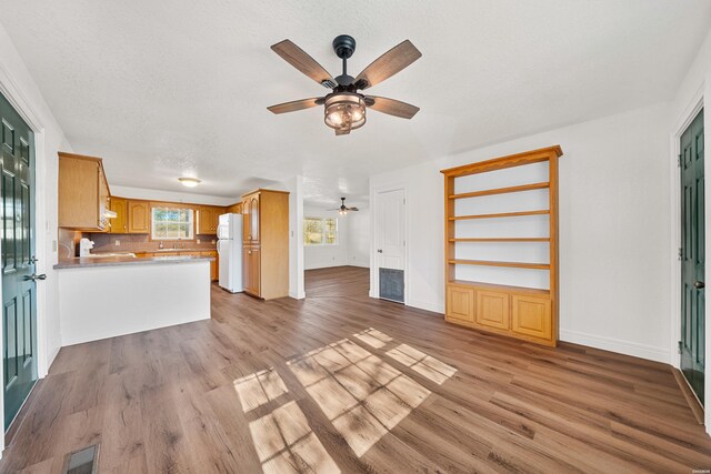 unfurnished living room featuring ceiling fan, a textured ceiling, light wood-style flooring, visible vents, and baseboards