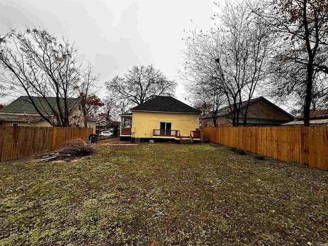 rear view of house with a shingled roof, a fenced backyard, a lawn, and a deck