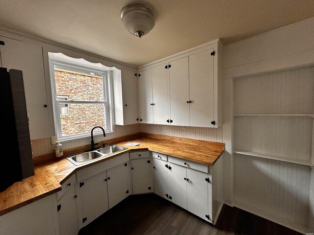 kitchen featuring dark wood finished floors, butcher block countertops, a sink, and white cabinetry