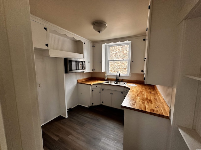 kitchen featuring butcher block countertops, stainless steel microwave, dark wood-style flooring, white cabinetry, and a sink