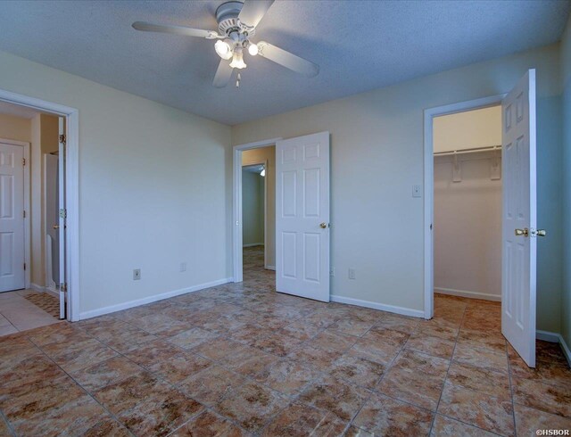 unfurnished bedroom featuring a textured ceiling, a closet, a walk in closet, and baseboards