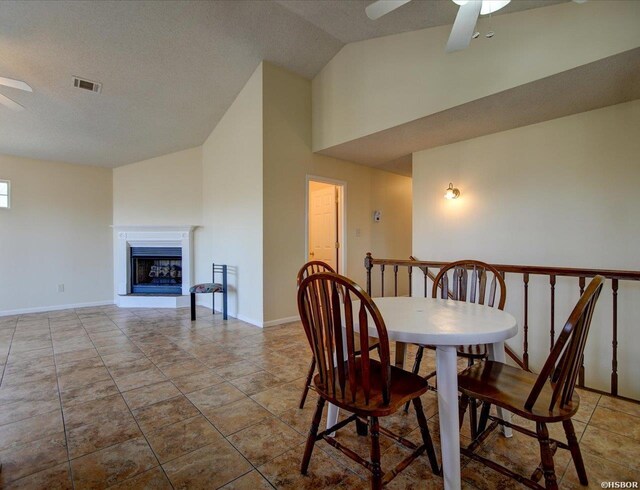 dining space featuring lofted ceiling, a fireplace with raised hearth, visible vents, baseboards, and a ceiling fan