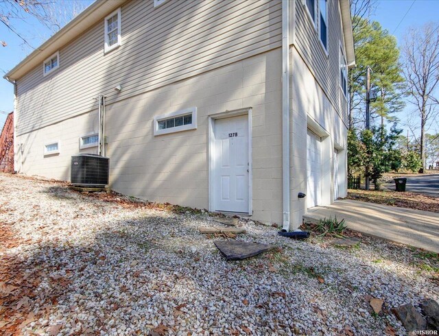 view of property exterior with a garage, concrete block siding, and central AC unit