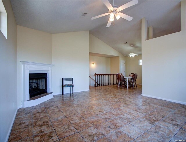 unfurnished living room with high vaulted ceiling, baseboards, a fireplace with raised hearth, and a ceiling fan