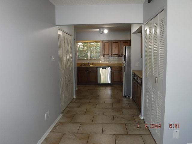 kitchen featuring brown cabinetry, decorative backsplash, stainless steel appliances, light countertops, and a sink