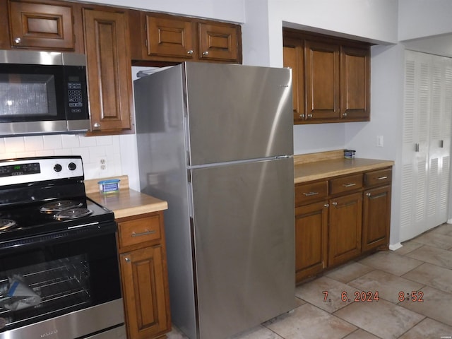 kitchen featuring appliances with stainless steel finishes, light tile patterned flooring, light countertops, and tasteful backsplash