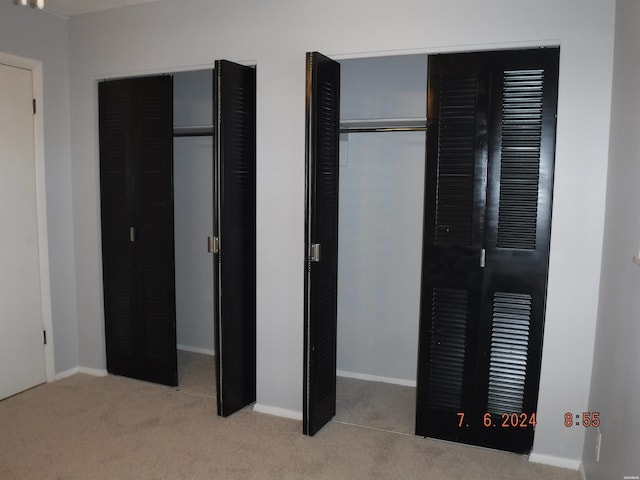 unfurnished bedroom with baseboards, a heating unit, multiple closets, and light colored carpet