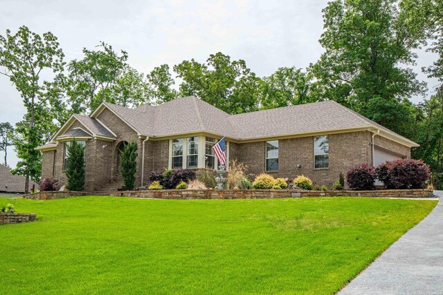 ranch-style home with roof with shingles, an attached garage, a front lawn, and brick siding