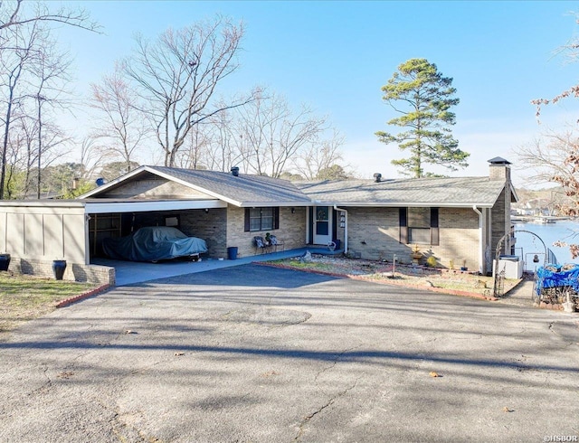 view of front of house featuring a chimney, aphalt driveway, a carport, and brick siding