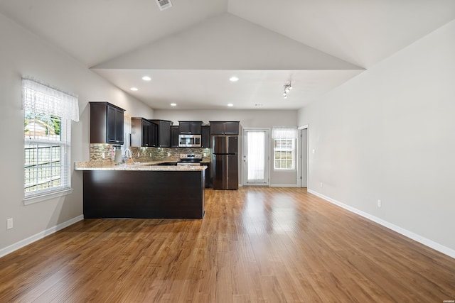 kitchen featuring tasteful backsplash, baseboards, appliances with stainless steel finishes, a peninsula, and light wood-type flooring