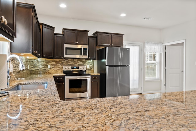 kitchen with dark brown cabinetry, stainless steel appliances, a sink, visible vents, and light stone countertops