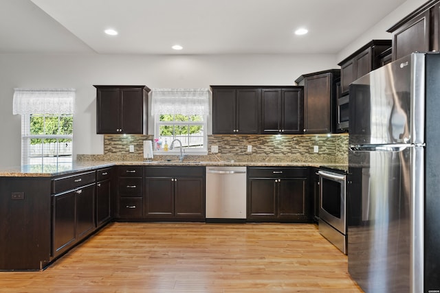 kitchen featuring stainless steel appliances, a sink, light stone countertops, light wood-type flooring, and a peninsula