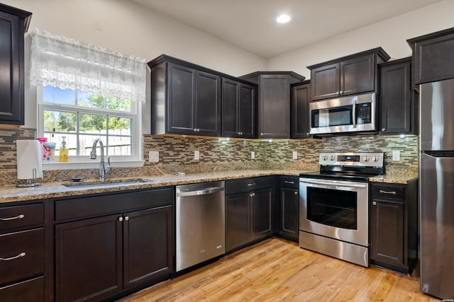 kitchen featuring light stone counters, a sink, appliances with stainless steel finishes, decorative backsplash, and light wood finished floors