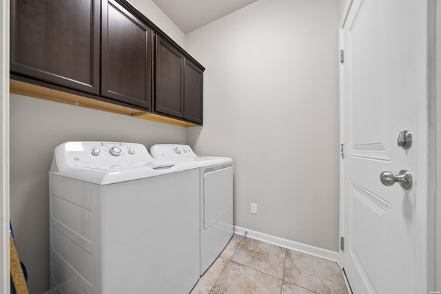 clothes washing area with light tile patterned floors, separate washer and dryer, cabinet space, and baseboards