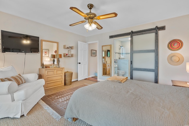carpeted bedroom with a barn door, ceiling fan, ensuite bathroom, and baseboards