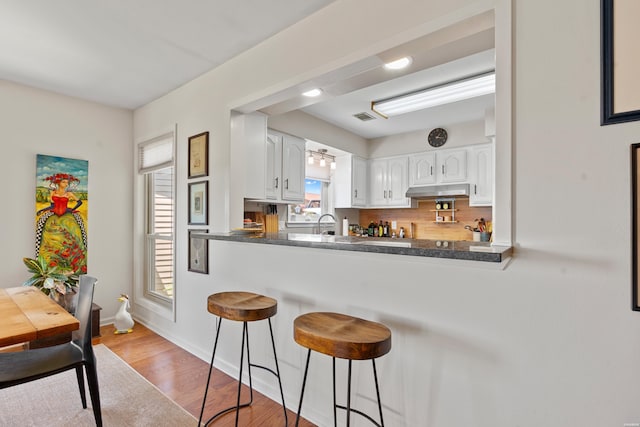 kitchen featuring wood finished floors, white cabinets, dark countertops, a kitchen bar, and visible vents