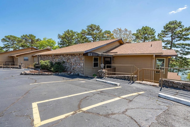 exterior space with uncovered parking, a shingled roof, and stone siding
