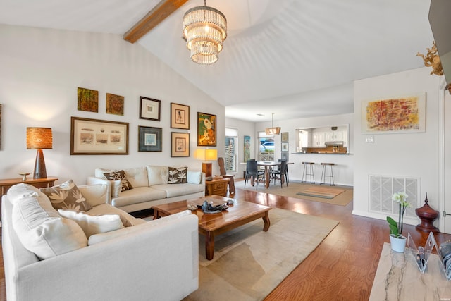 living area featuring lofted ceiling with beams, a notable chandelier, visible vents, and wood finished floors