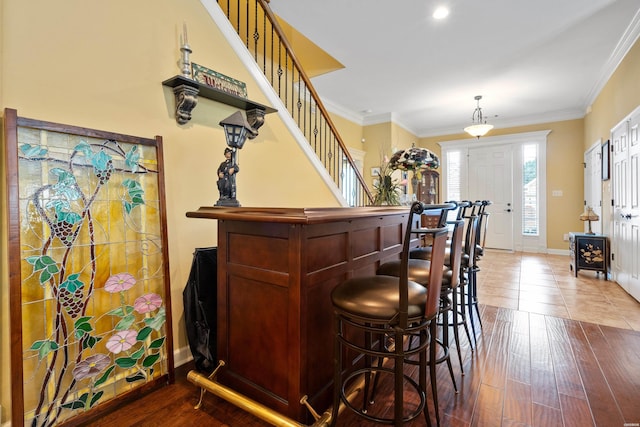 bar featuring ornamental molding, wood finished floors, baseboards, and stairs