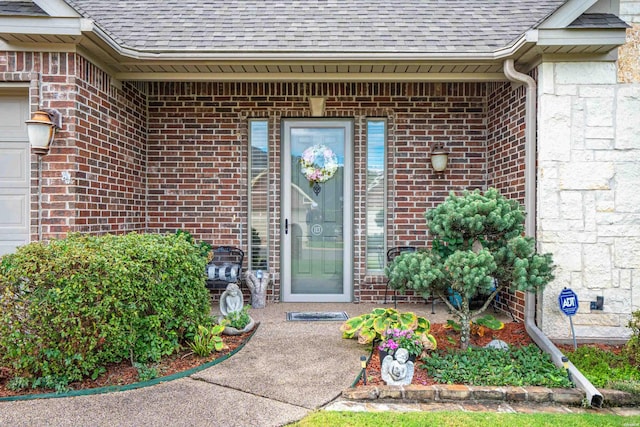 entrance to property with an attached garage, stone siding, a shingled roof, and brick siding