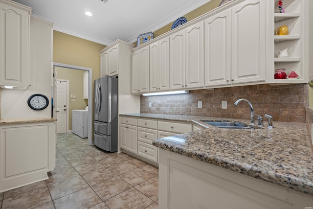 kitchen with crown molding, freestanding refrigerator, white cabinets, a sink, and light stone countertops