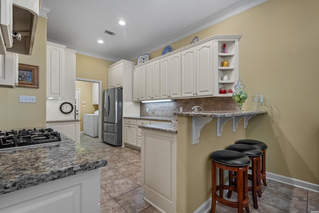 kitchen with stainless steel appliances, white cabinets, dark stone counters, open shelves, and a kitchen bar