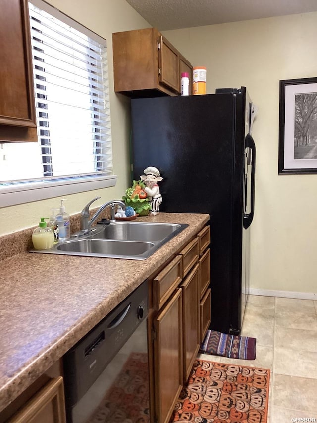 kitchen featuring stainless steel dishwasher, freestanding refrigerator, a sink, a textured ceiling, and baseboards