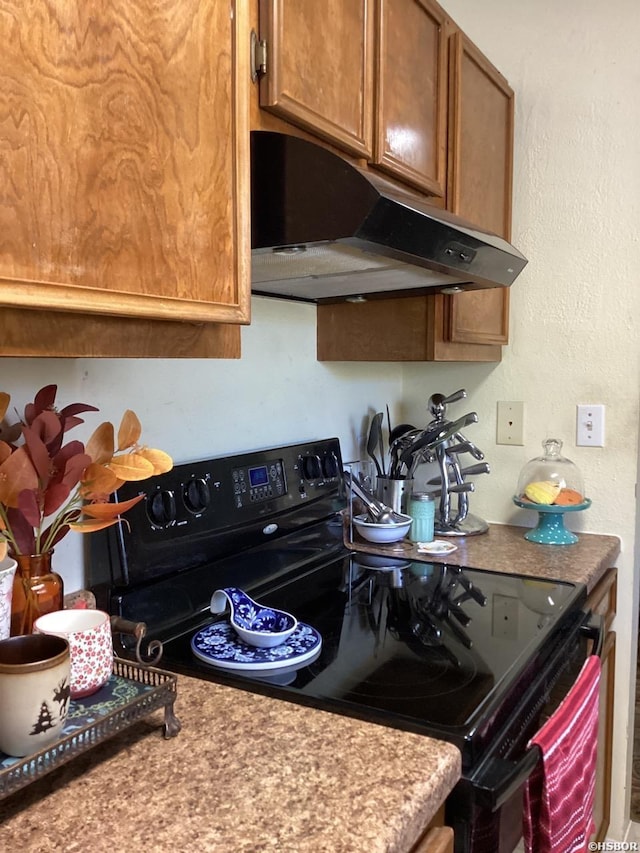 kitchen with a textured wall, brown cabinets, black / electric stove, light countertops, and under cabinet range hood