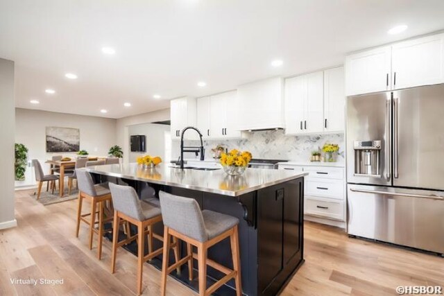 kitchen with high end fridge, white cabinetry, a sink, and an island with sink